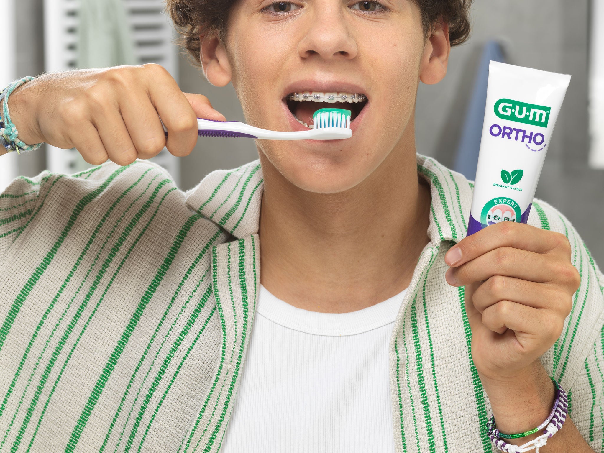 smiling teen with brackets while he's holding the GUM ORTHO toothbrush and toothpaste