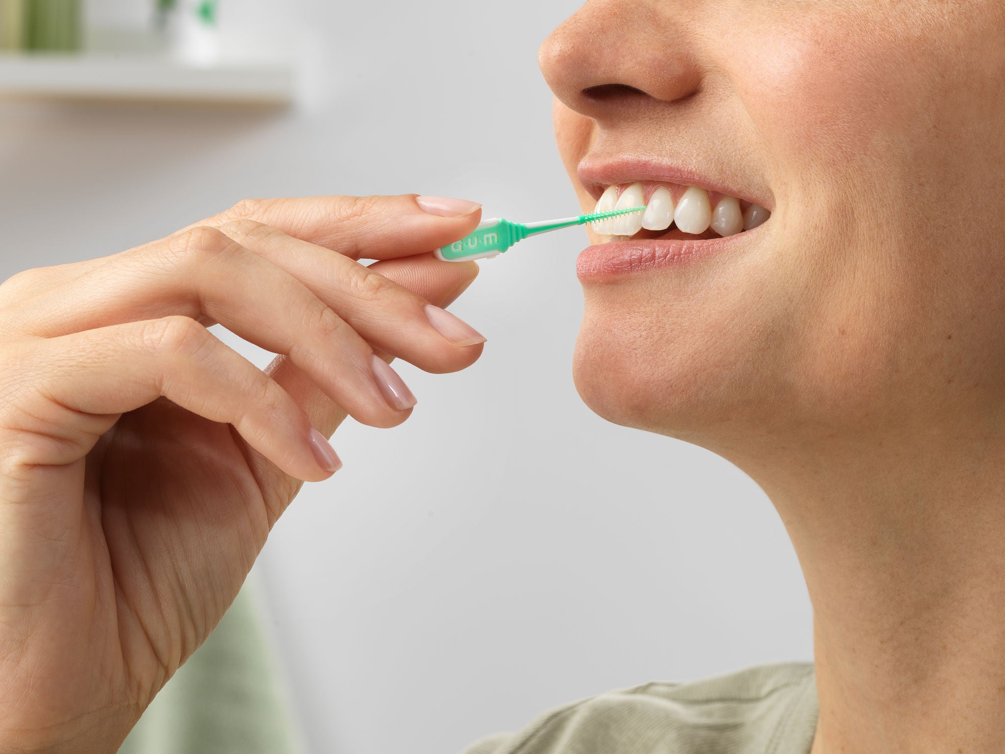 Smiling woman is cleaning between her teeth with the GUM SOFT-PICKS MINTY Interdental brush 