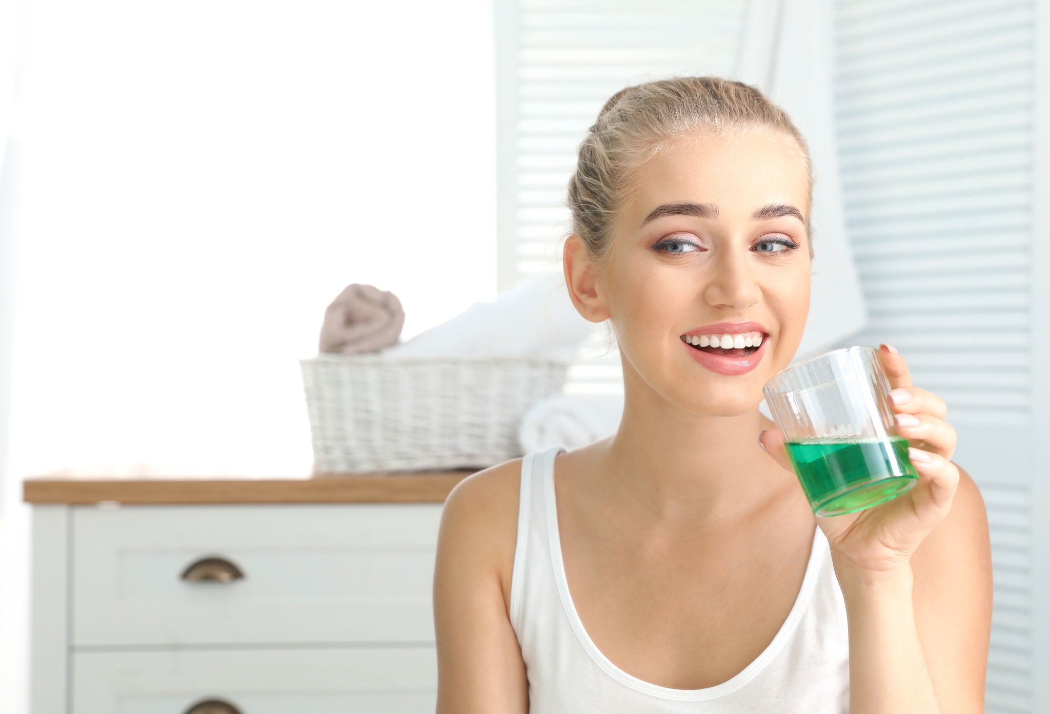 Woman holding glass with mouthwash in bathroom. Teeth care