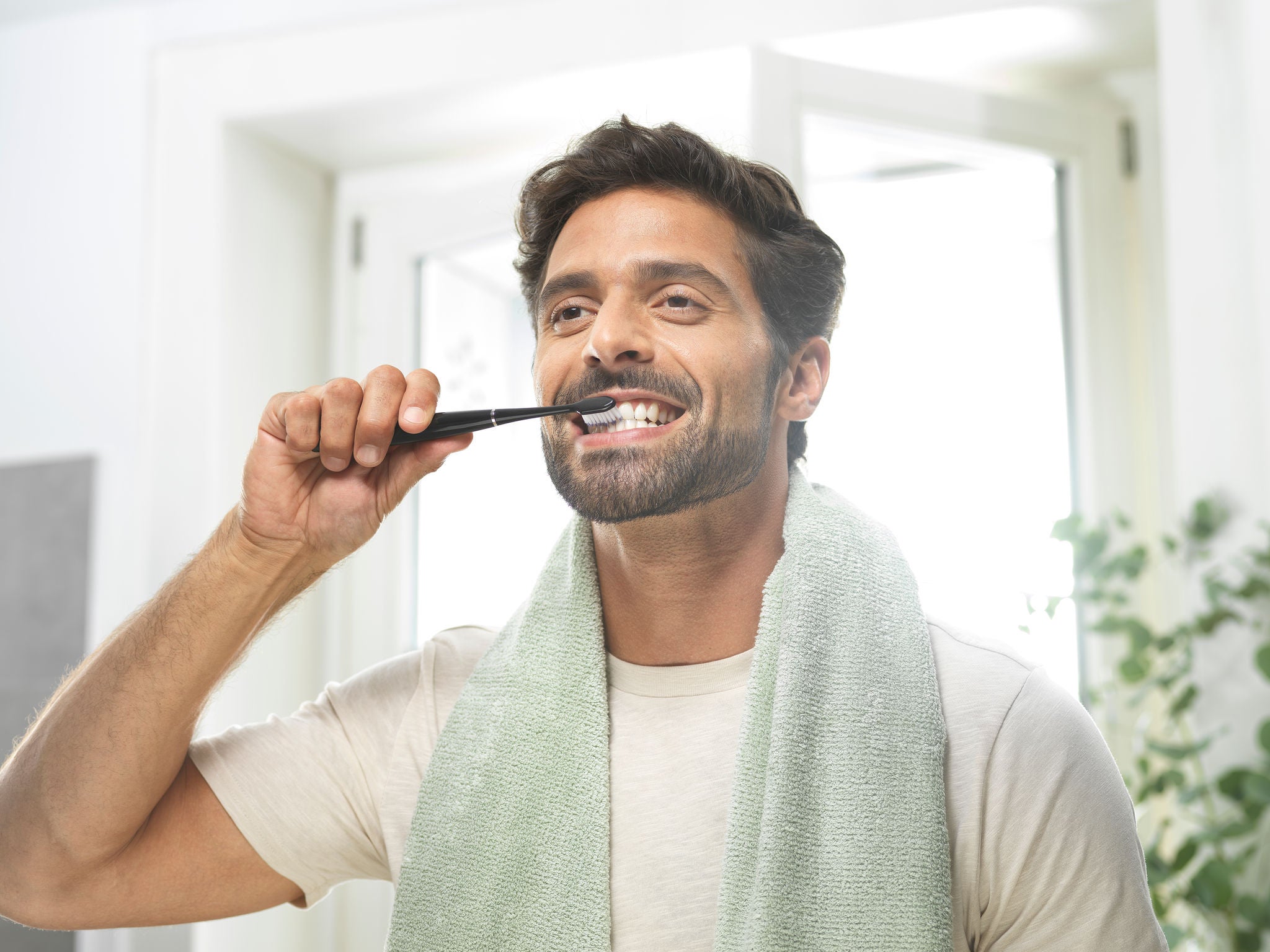 Smiling man is brushing his teeth with the GUM SONIC DAILY toothbrush, the black one