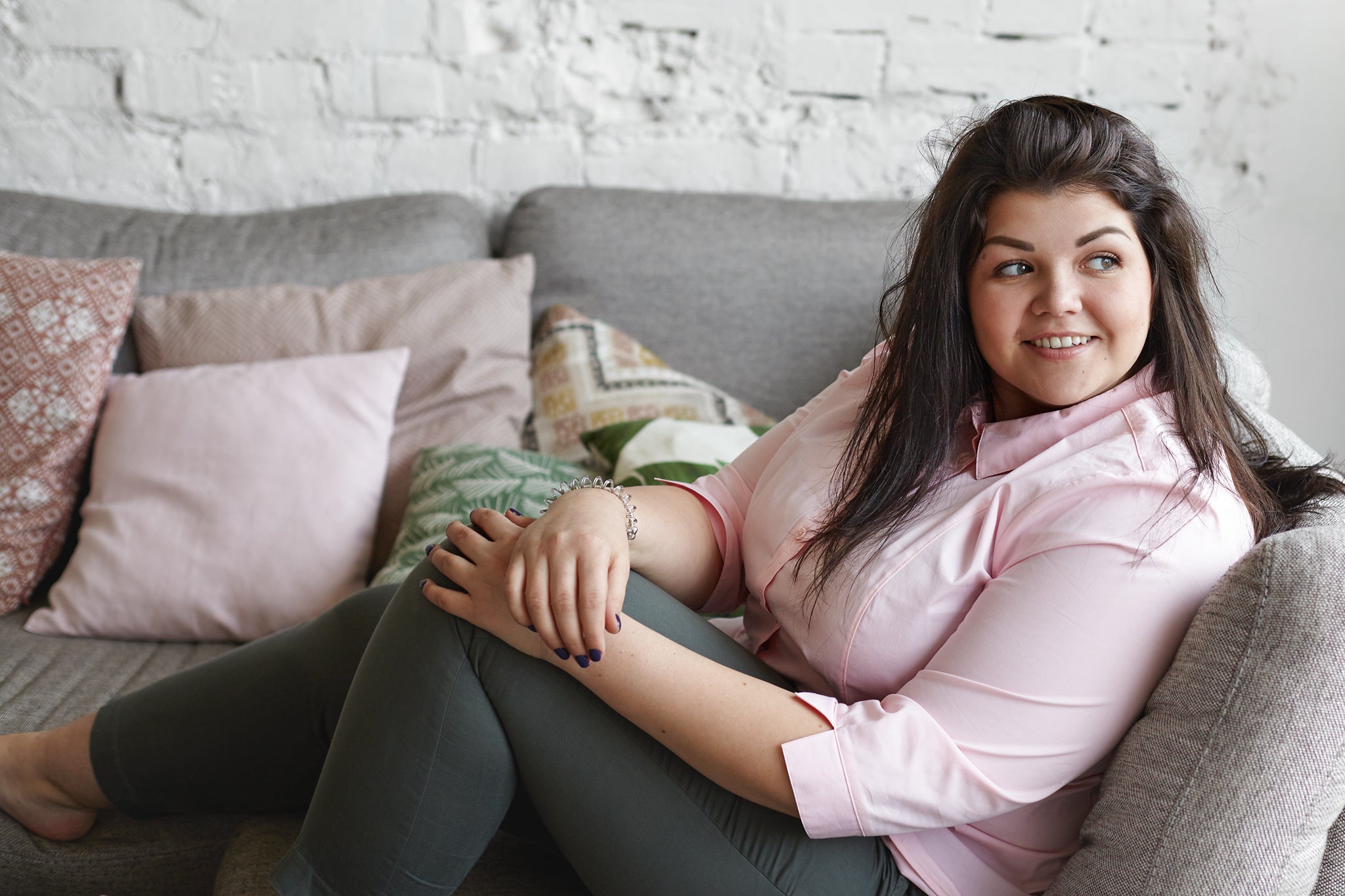 Plus size woman sitting on sofa pink shirt brown hair 