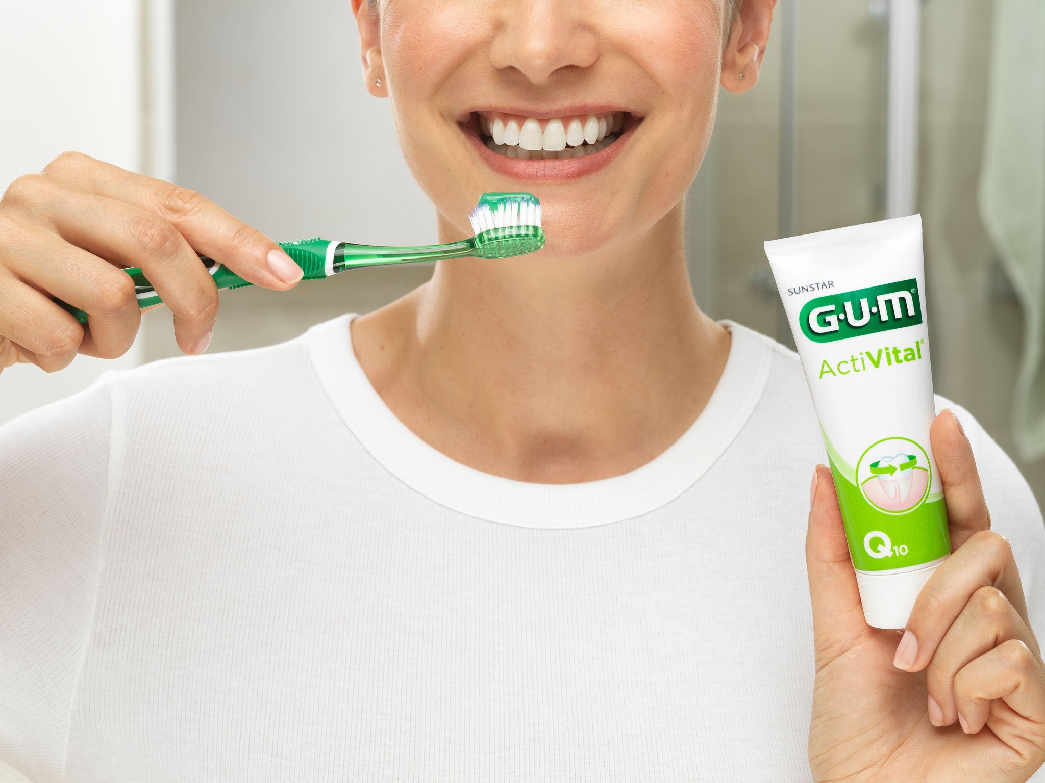 Smiling Woman is starting brushing the GUM PRO toothbrush while she's also holding the GUM Activital toothpaste