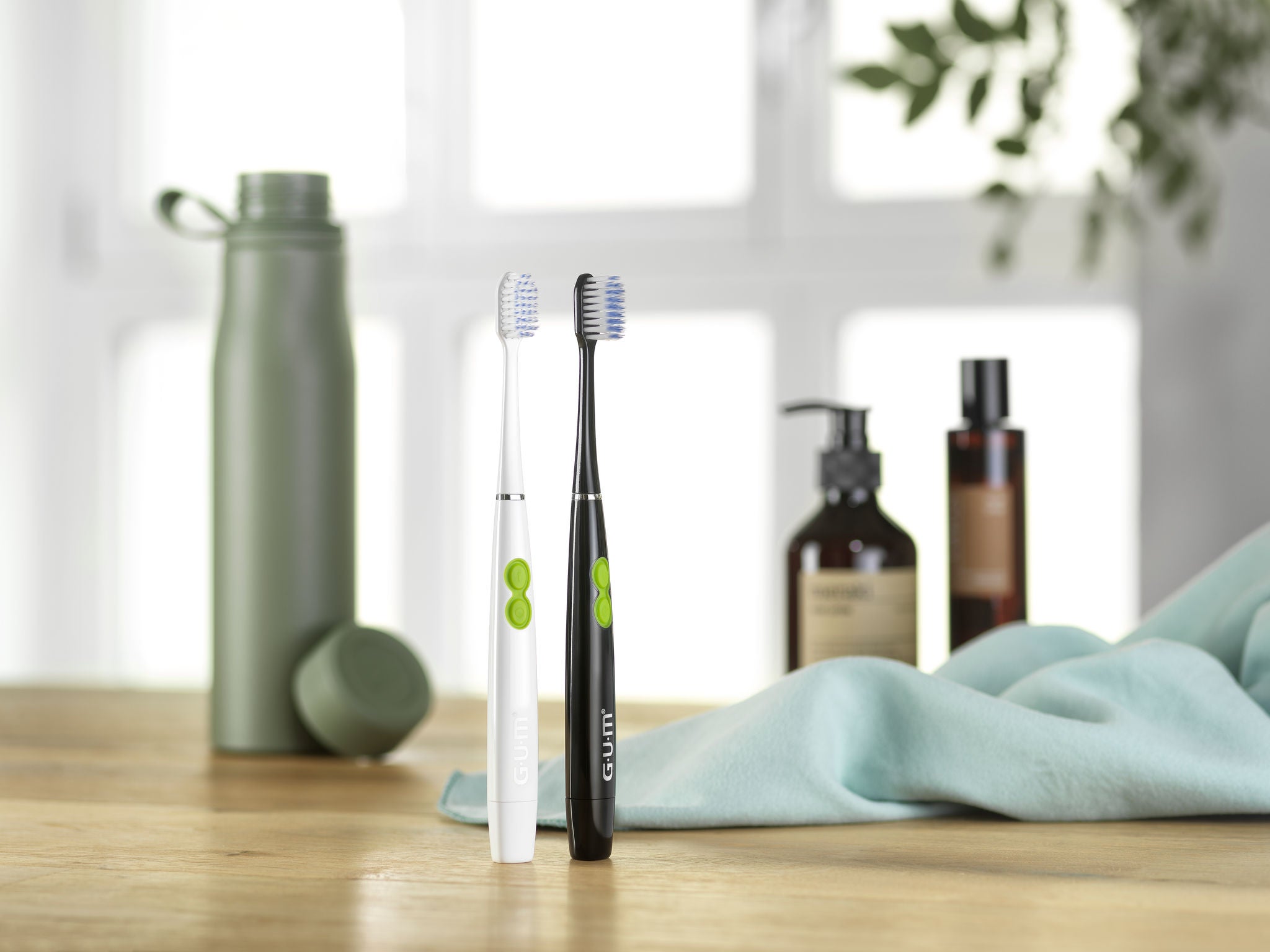 GUM SONIC DAILY toothbrushes standing up and some beauty elements in the background with a green towel