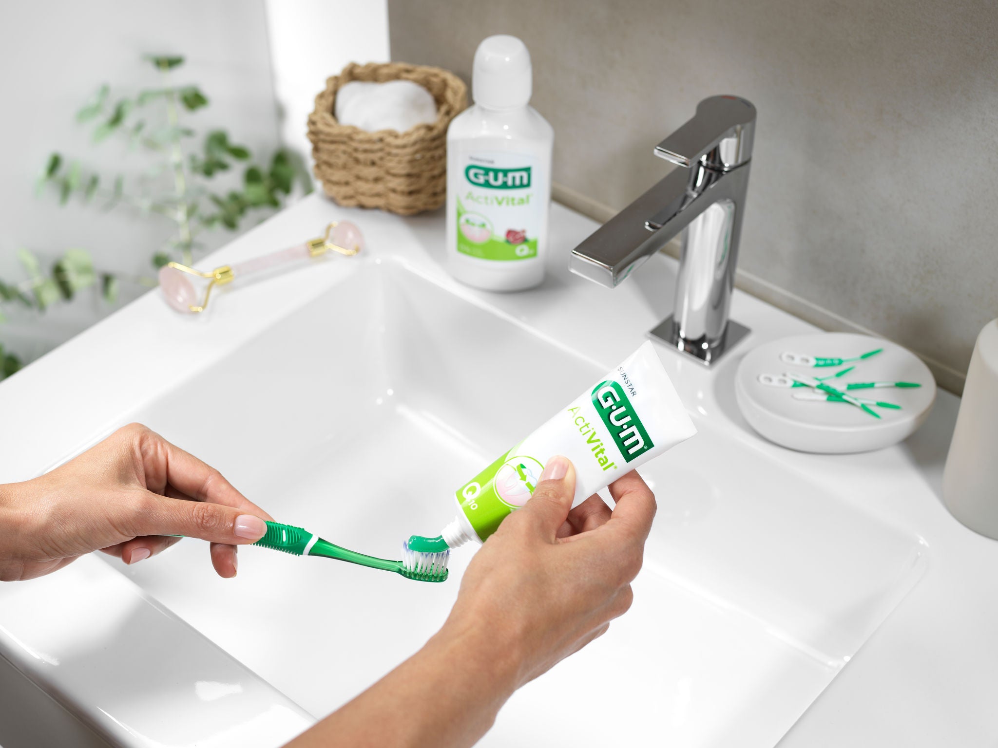 Woman is putting the GUM ActiVital toothpaste on the GUM PRO toothbrush to start brushing her teeth and other GUM products are in the background