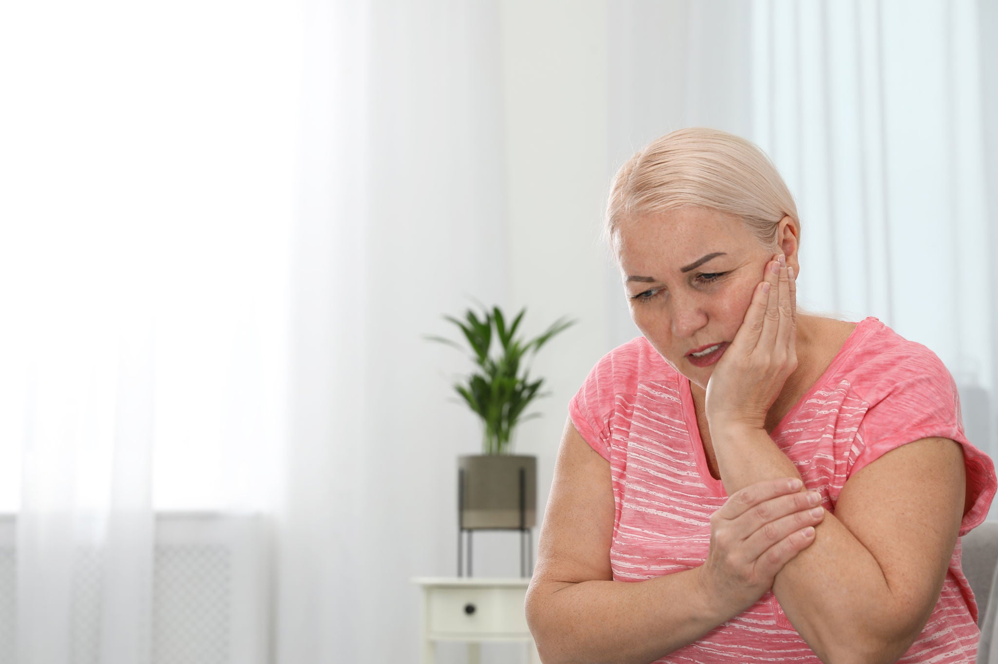 Mature woman suffering from strong tooth pain at home, space for text