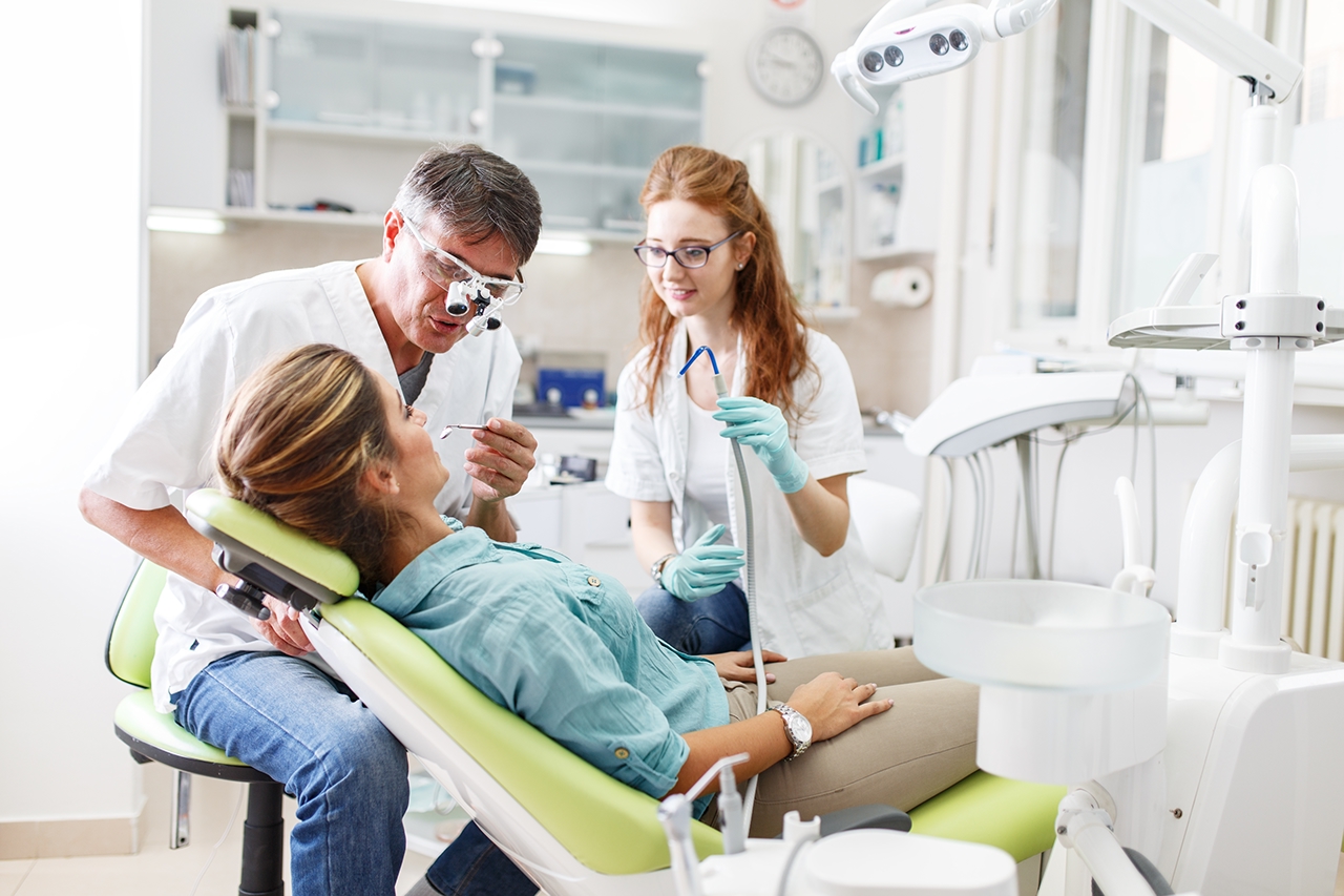 Senior male dentist in dental office talking with female patient and preparing for treatment. man woman
